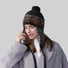 Woman wearing black wool-acrylic ear flap hat with orange Fair Isle patterns and a playful pom-pom.