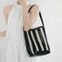 Model carrying the small black and white striped raffia bucket bag as shoulder bag.