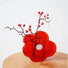 Angled view of Red acrylic flower-shaped vase with berry branch on wooden table.