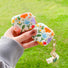 Model Hands holding two Flowers AirPods Case Covers, easy to carry for commutes and travel.