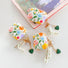 Three silicone AirPods cases with colorful floral print, lace ribbon, and green heart charms.