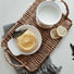 Front view of Hand-woven rattan tray with handles, holding a white mug, lemon pastry, and slices.