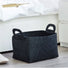 A black storage basket with handles sitting on a floor next to a white cabinet.