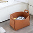 A tan felt storage basket containing books, placed next to a bed.