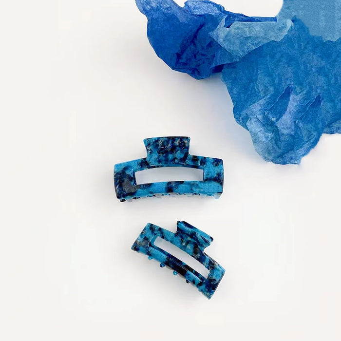 Two Midnight Ice acrylic hair claws shown together, with blue and black marbled patterns.
