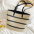 Front view of Woven straw tote bag with black stripes, black PU leather handles, and a zipper closure.